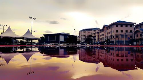 Buildings by lake against sky during sunset