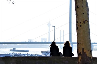 Rear view of women sitting on bridge against sky