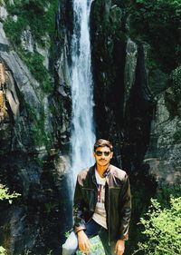 Portrait of young man standing against waterfall