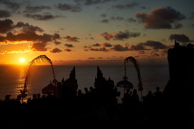 Silhouette buildings by sea against sky during sunset