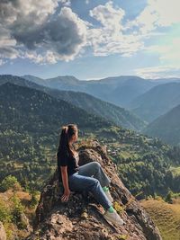 Woman sitting on mountain against sky