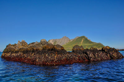 Rock formation in sea against clear blue sky