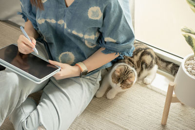 Asian woman play with her cat and use tablet meeting and working from home