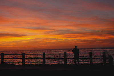 Silhouette man standing by railing against sea during sunset