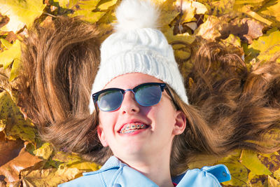 Teenager girl wearing sunglasses and cap is lying down on the floor covered by yellow leaves while enjoying the sunny day. the brunette girl is happy and smiling. horizontal photo