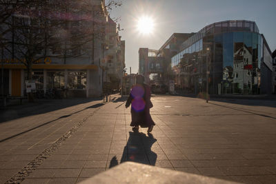 Rear view of woman walking on sidewalk by buildings in city