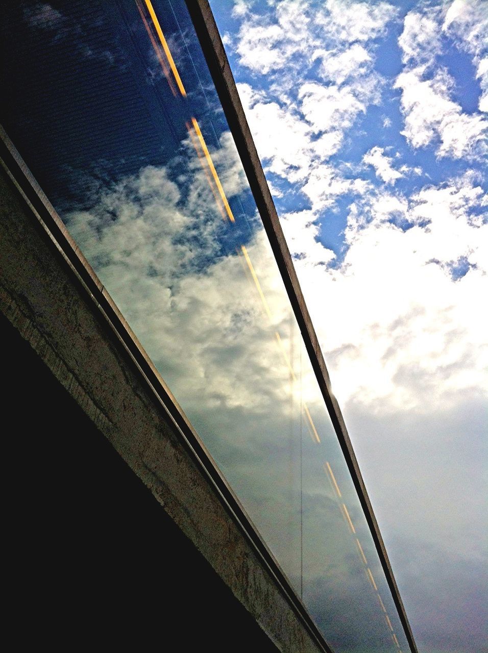 low angle view, sky, architecture, built structure, cloud - sky, cloud, transportation, cloudy, connection, window, building exterior, day, glass - material, no people, reflection, outdoors, railing, part of, modern, bridge - man made structure