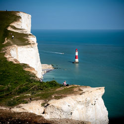 Woman watching lighthouse by sea against sky