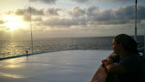 Side view of woman in boat on sea against sky during sunset