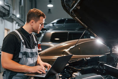 Side view. man in uniform is working in the auto service.