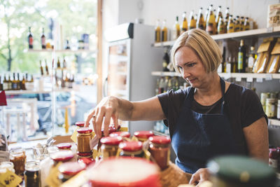 Mature female employee arranging jars in deli