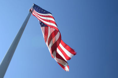 Low angle view of american flag waving against clear blue sky