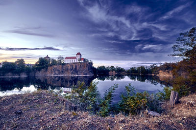 Buildings by river against cloudy sky