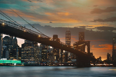 Illuminated bridge over river against sky during sunset