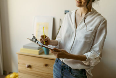 Mid adult woman writing with pen on clipboard