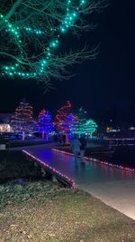 Illuminated city by river against sky at night