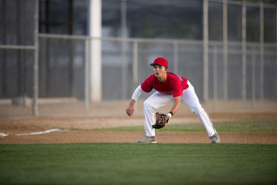 Teen baseball player in red uniform ready for a ground ball