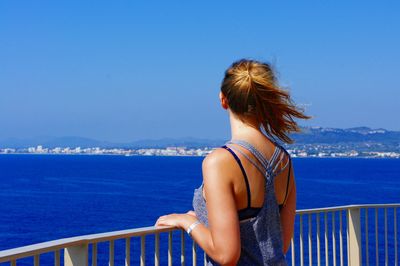 Rear view of young woman by railing looking at sea on sunny day