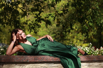 Young woman sitting on plant against trees