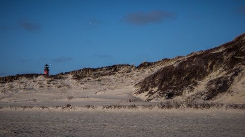 Distant view of lighthouse by mountain at beach against sky