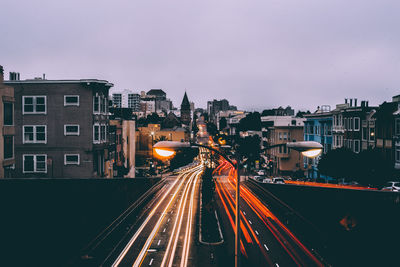 Light trails on road amidst buildings against sky at dusk