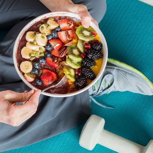 A large fruit smoothie bowl with person eating while sitting on a yoga mat.