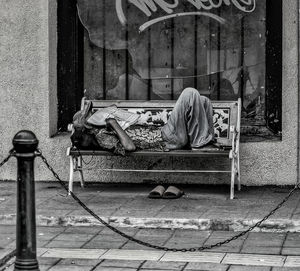 Homeless man sleeping on bench in city