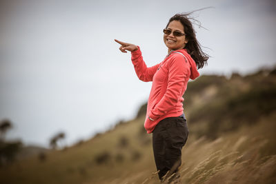 Young smiling woman pointing while standing on grassy hill