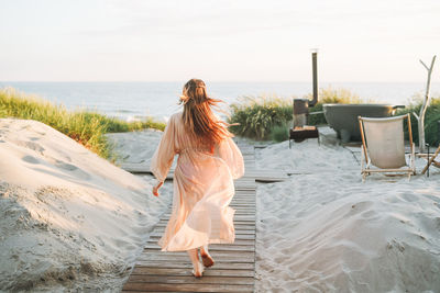 Rear view of woman with arms raised standing at beach