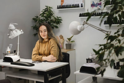 Nail service master. portrait of professional young brunette sitting at modern nail salon workplace