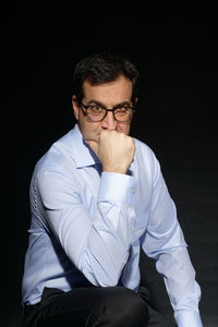 Young man looking away while sitting against black background