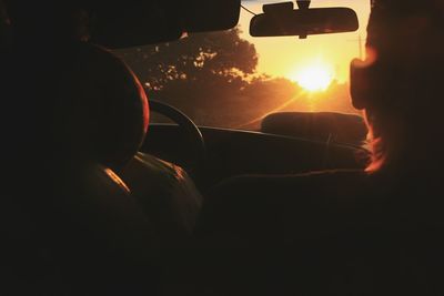 Rear view of silhouette man driving car against sky during sunset
