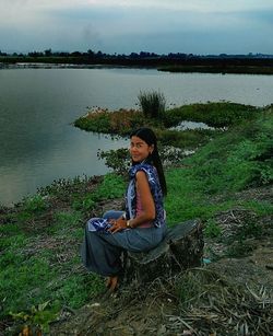 Portrait of smiling young woman sitting on lake against sky