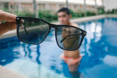 Reflection of man holding sunglasses in swimming pool