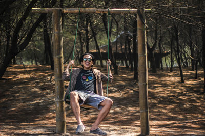Portrait of young man sitting on swing in forest