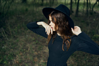 Side view of young woman standing against trees