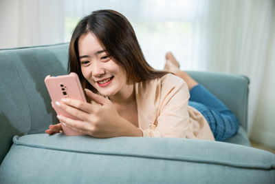 Young woman using mobile phone while sitting on sofa at home