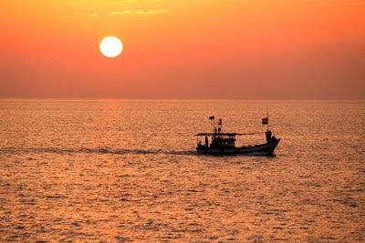 Silhouette boat sailing in sea against orange sky