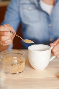 Midsection of woman holding brown sugar and cup of coffee