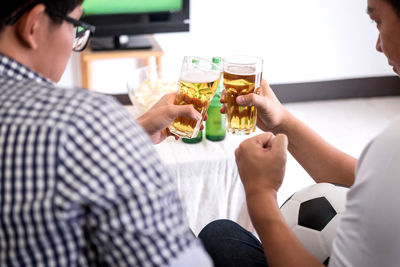 Rear view of friends toasting beer bottles while watching sports on tv at home