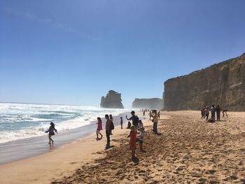 People walking at beach against clear sky