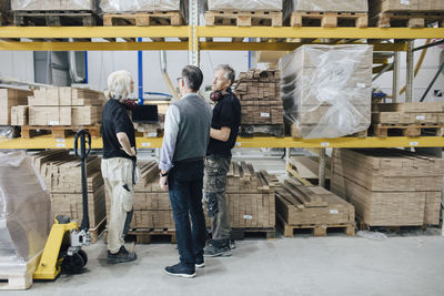 Full length of business people planning over wooden planks while standing in industry