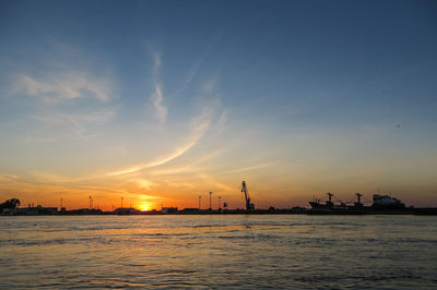 Silhouette city by sea against sky during sunset