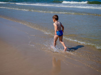 Young happy boy running on the baltic sea beach during sunny summer day