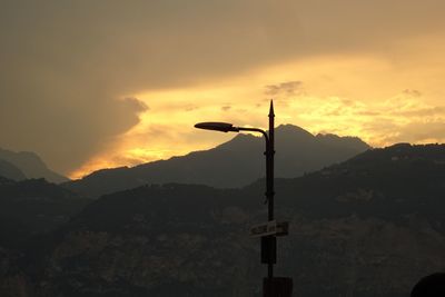 Silhouette cross on street against sky during sunset