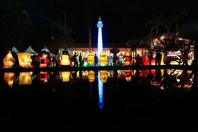 People at illuminated city against sky at night