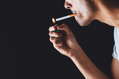 Midsection of man holding cigarette against black background