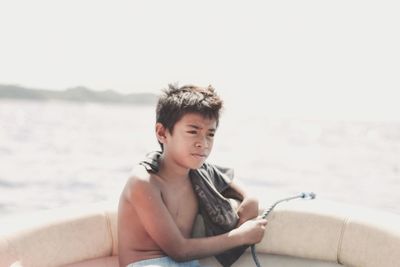 Boy sitting in sea against sky