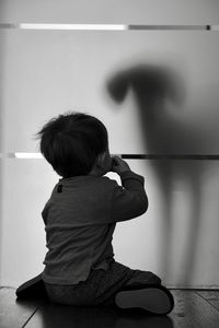 Rear view of boy sitting on wall at home