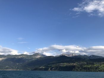 Scenic view of sea by mountains against blue sky